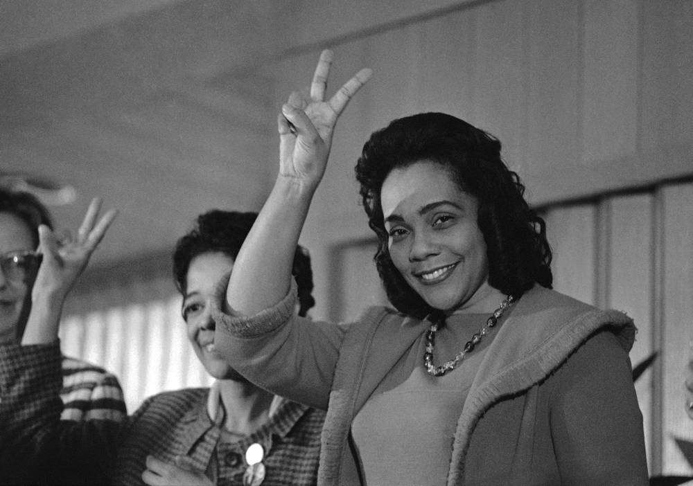 Photograph of Coretta Scott King smiling and holding up a peace sign with her fingers.