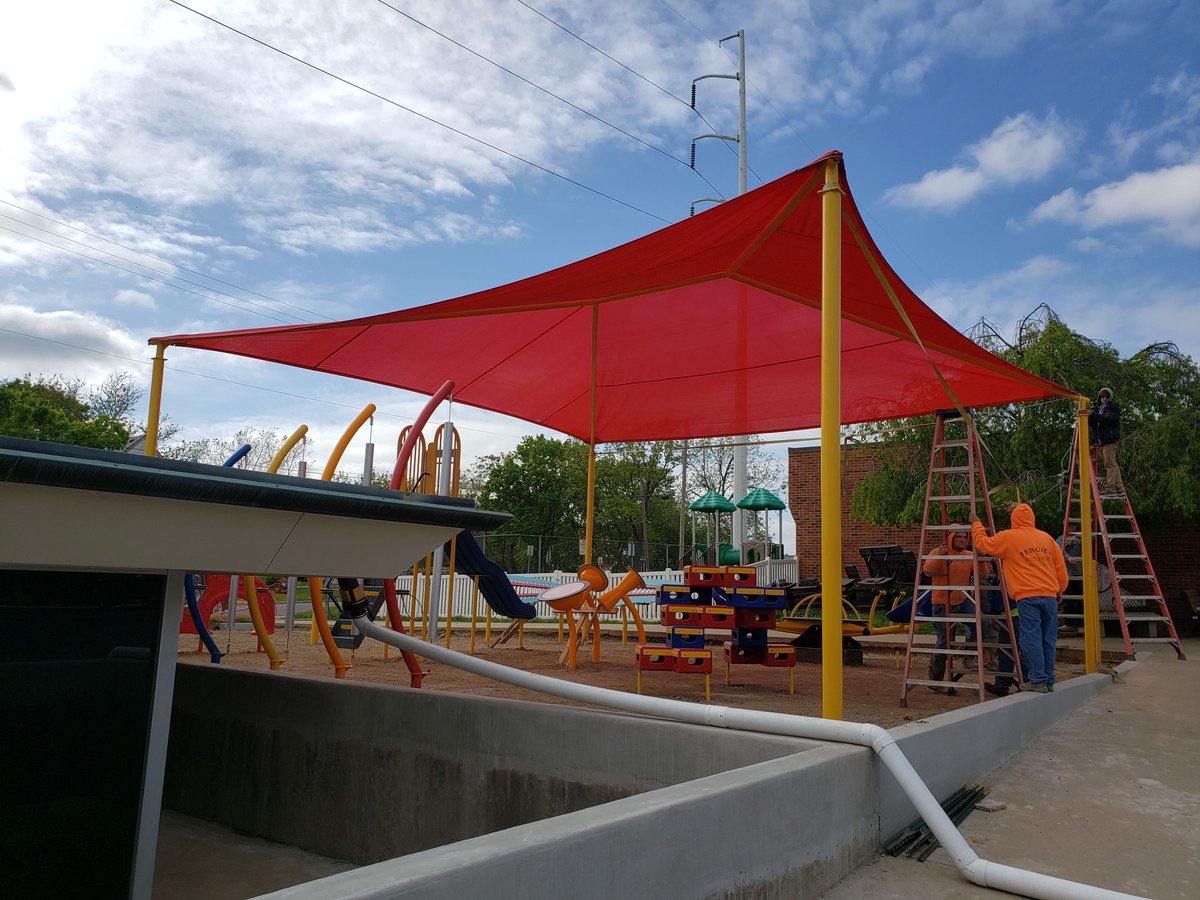 A large red awning resting on 4 yellow poles covers new playground equipment.