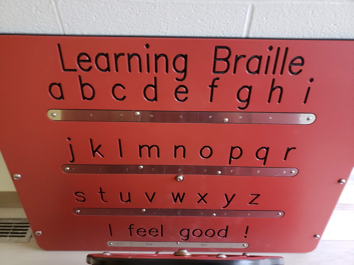 A red playground sign that says "Learning Braille" with the letters of the alphabet in print and braille.