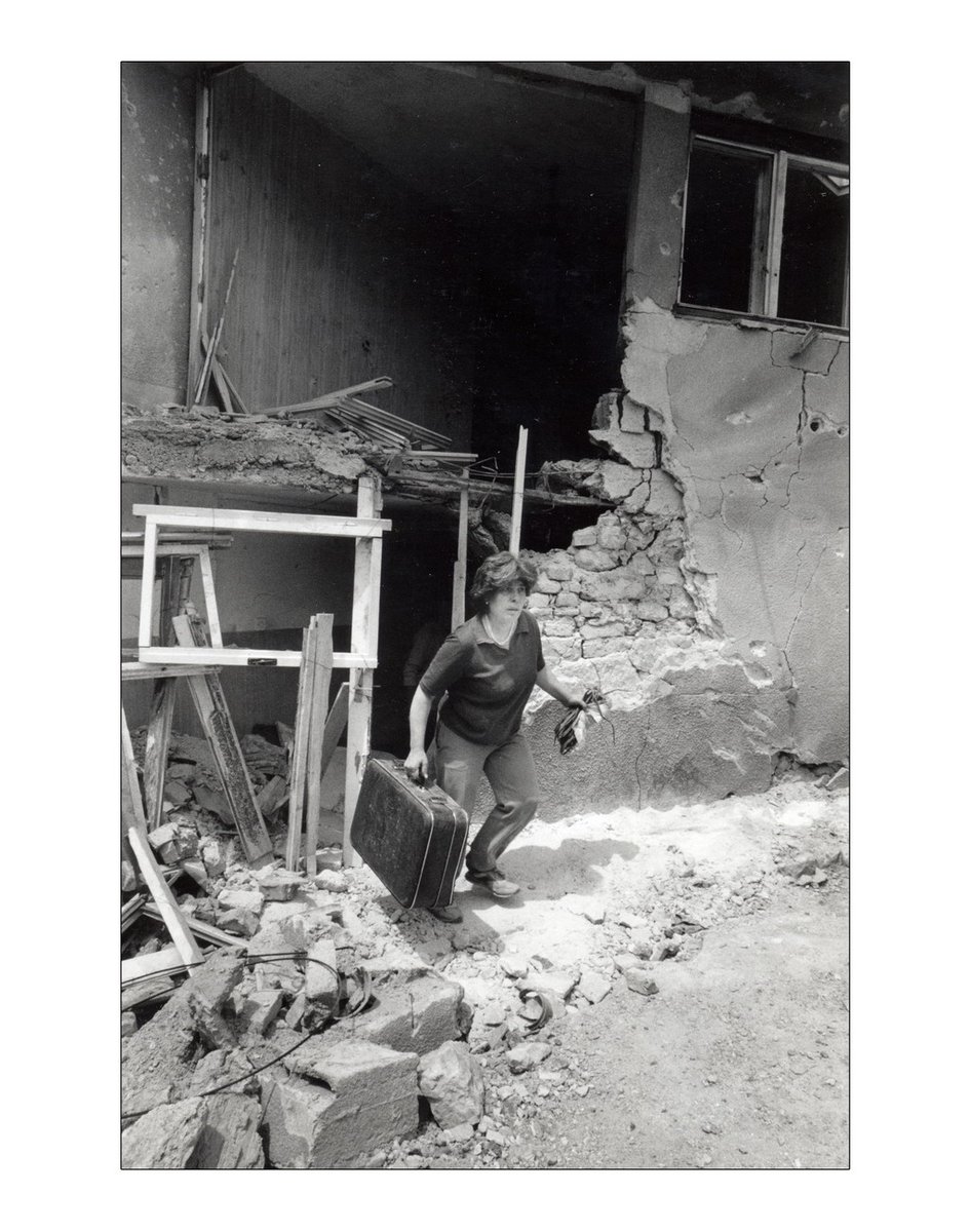 DAILY ROUTINE. The old quarter of the city is attacked with rocktes. The walls of the houses fall down as if they were made of cardwood. A woman leaves her home nwith a case containing the few things she has managed to sabe  @BosnianHistory  @slyon66  @EFM1959  @perezreverte