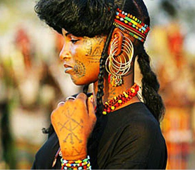 Une tresse enroulée autour du périmètre de la tête ;Des perles, cauris (coquillages), pinces dorées éparpillées un peu sur toutes les tresses.cette coiffure exprimait le statut social, la situation matrimoniale ou l’appartenance ethnique des femmes qui l’arboraient.