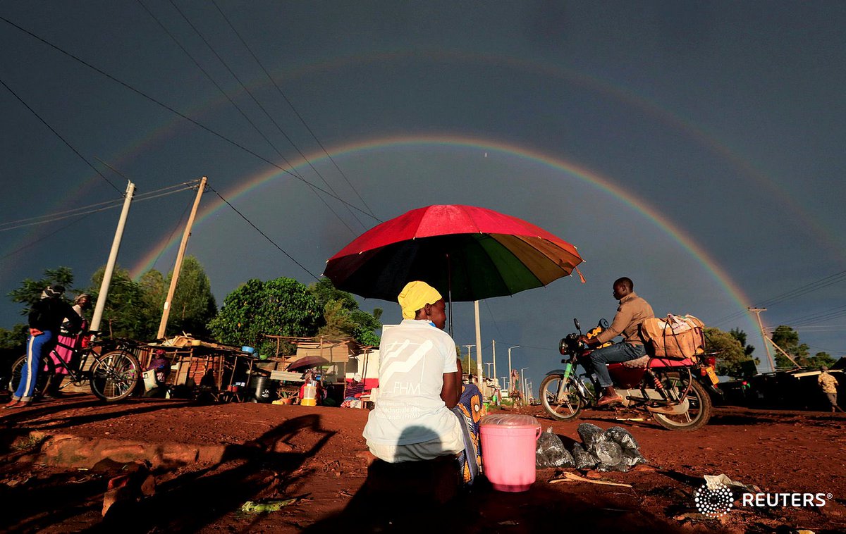 A double rainbow is seen above a woman holding an umbrella and selling snacks along the road in Siaya county, Kenya