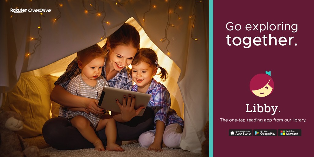 a woman under a blanket fort smiling, holding two small children while also showing them a tablet