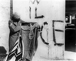 A Sikh soldier (of the 4th Division (the Red Eagles) of the Indian Army), holding a captured swastika flag after the surrender of Nazi German forces in Italy.Behind him, fascist inscriptions on the mural says VIVA IL DUCE, "Long live the Duce" (Benito Mussolini).May 1945.