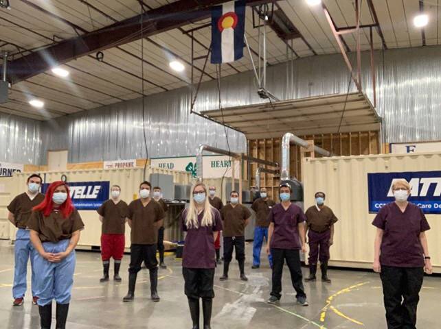 A dozen people standing in a room in front of large metal containers
