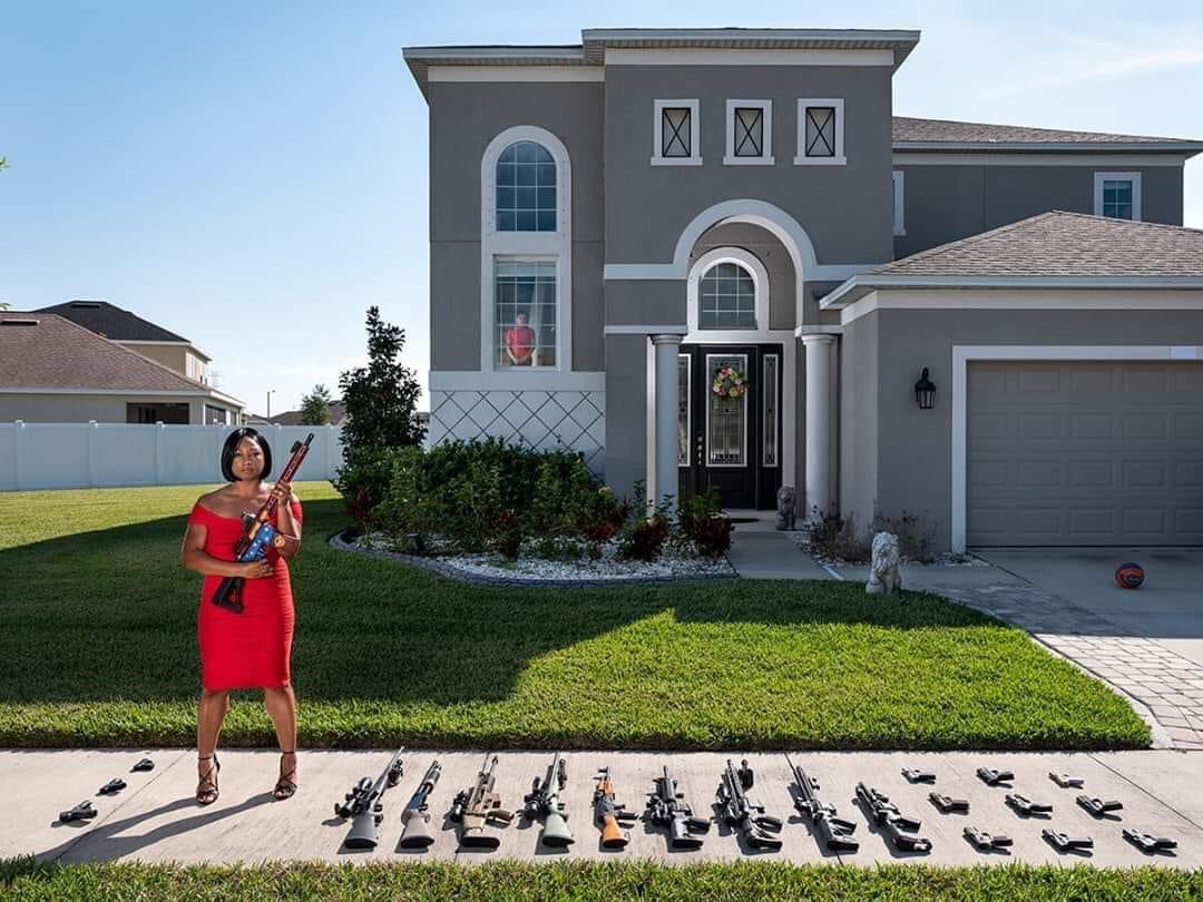 POWERFUL—Black woman stands outside of her home posing with all the firearms she owns to protect her son (standing in window) and family. So, where’s the husband? He’s taking the photo of the lady in red dress. #AhmaudArbery #2A #2ndAmendment #GunRights #GunSense #NRA 🇺🇸