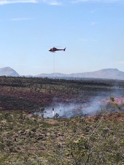 Helicopter with a long line and bucket of water cooling hotspots on the Basin Fire.