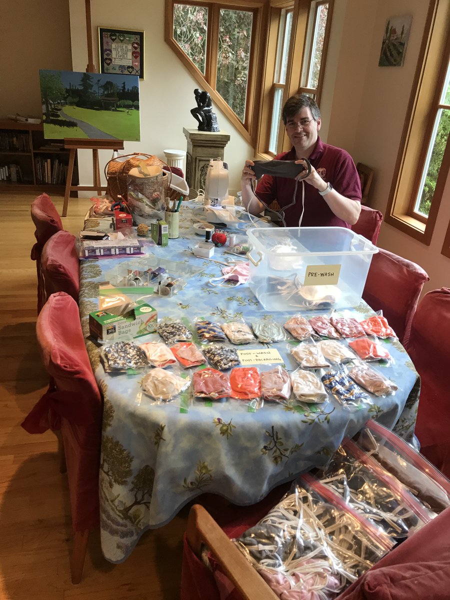 A person sits at a dining room table filled with fabric face coverings.