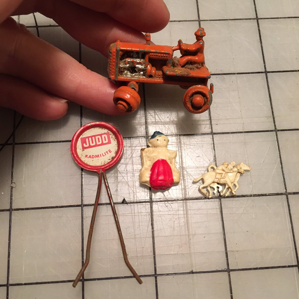 These are c. 1950. The Judd Kadmilite pin is a hardware store display for eye- hooks, the two-sided molded plastic charms and the cast metal toy tractor are all c. 1950 toys.