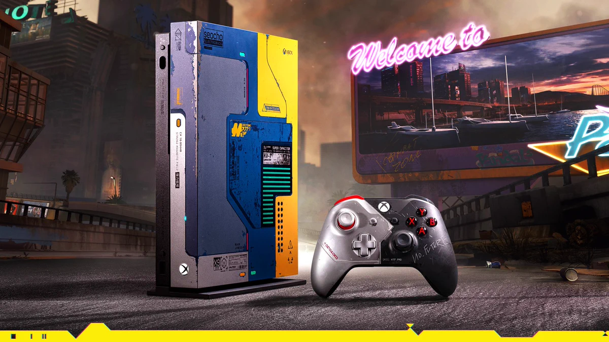 In the foreground sits the Xbox One X Cyberpunk 2077 Limited Edition console and controller. The console is standing upright and has shades of blue and yellow. The controller is half silver, half black with red accents, and 'No Future' is scratched into it. The backdrop is of Night City, replete with high rises, an overpass and a billboard welcoming guests to the city.