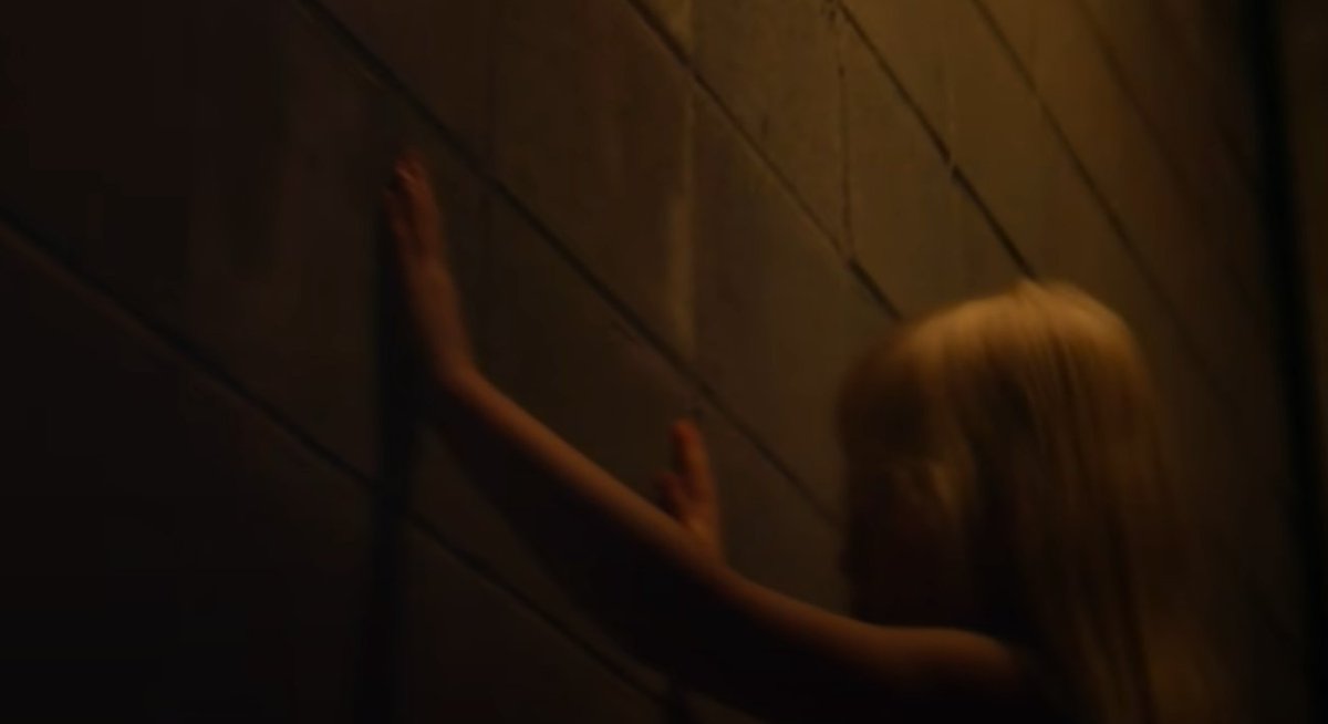 Back to the video, shortly after the headshots is one of the first creepy shots with what looks like a young girl with her hands on a brick wall (basement/warehouse look) as if she were being sold or trafficked (or worse)