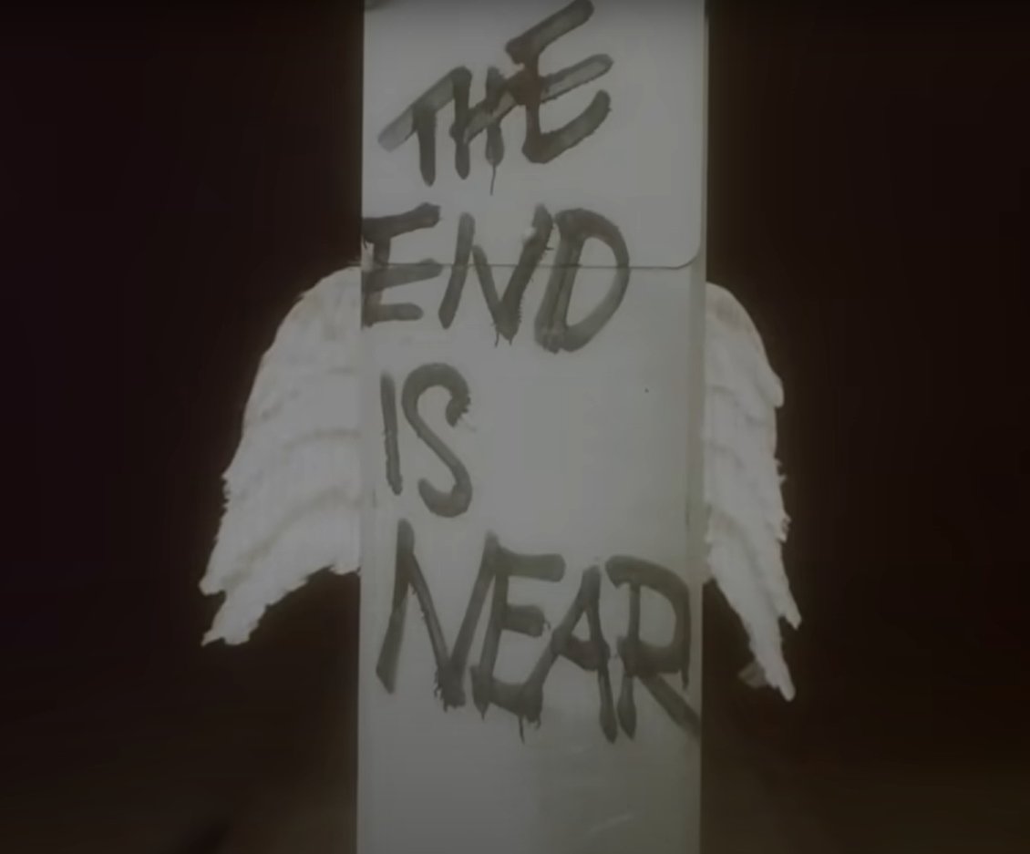 Shot of column with "The End is Near" sprayed on it and angel wings appearing on either side. This can serve as a warning to people, or as a light at the end of the tunnel (Like saying "Have faith, its almost done")
