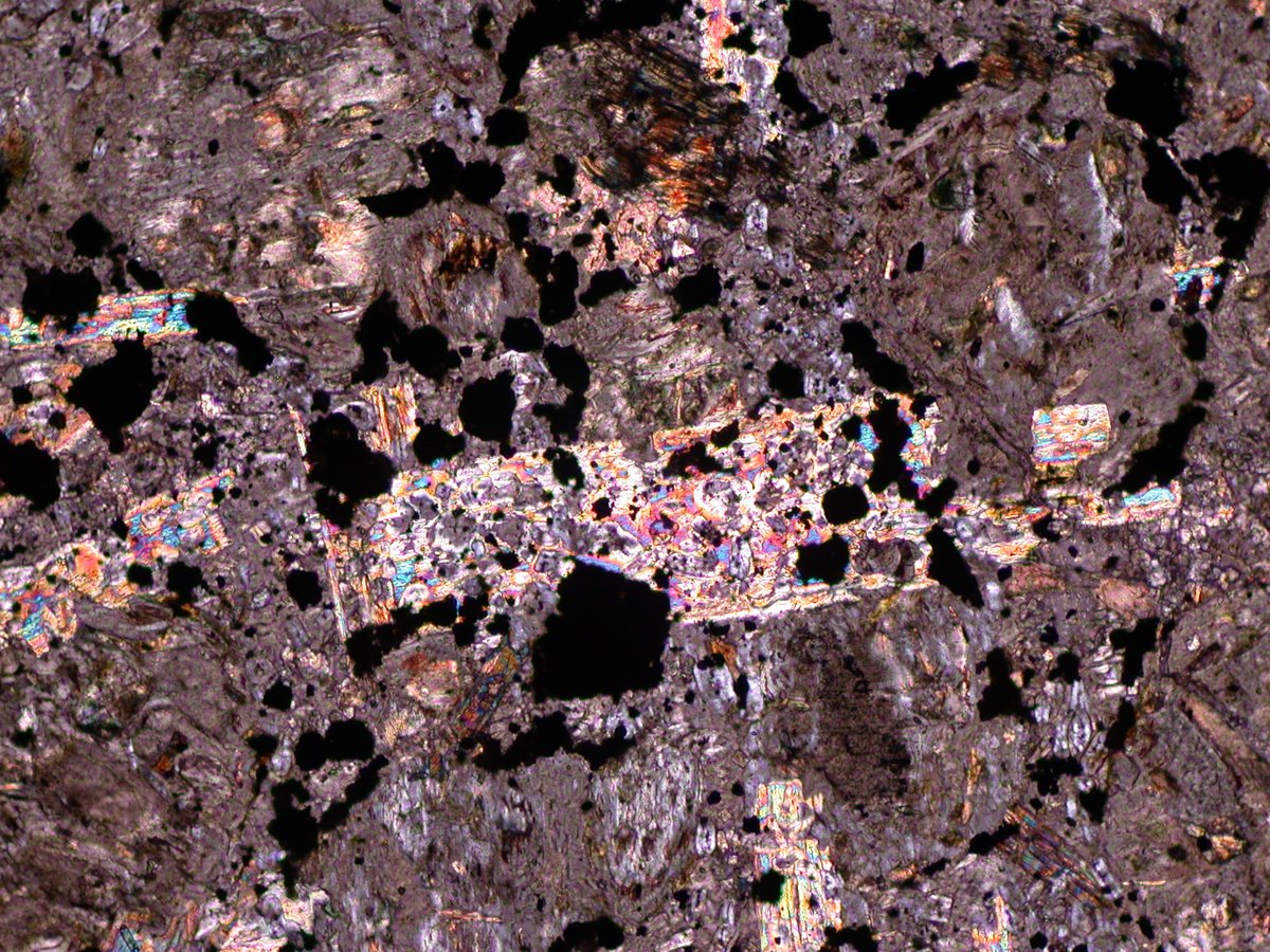 NARminerals's tweet photo. Thurs School of Rock w/ #GeoDan! "Checking out a phlogopite x-tal w/ poikilitic texture; it shows 2nd order birefringence (colorful) & has x-tallized around & encased perovskite & monticellite x-tals (opaque & pale grey) in this #kimberlite groundmass. FOV 1.5mm PP & XPL". https://t.co/di9cIdISSO