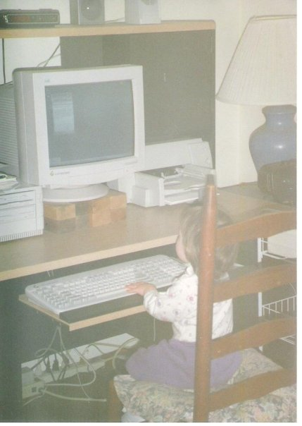A 2 year old sitting on a chair in front of a computer in 1997. One hand is on the keyboard.