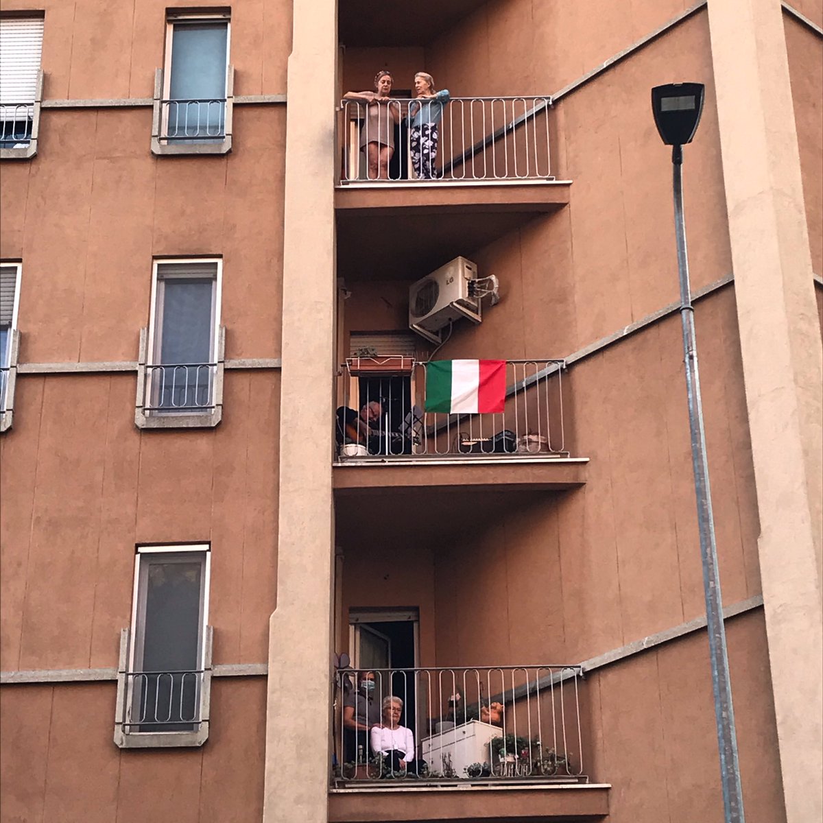 . #17maggio2020 Milano, Quartiere Calvairate. 
Il signor Enzo, qui nascosto dalla bandiera italiana, canta Vecchioni, De Andre’, e gli altri grandi, mentre vicini e passanti cantano e lo applaudono. #buonadomenica #fase2