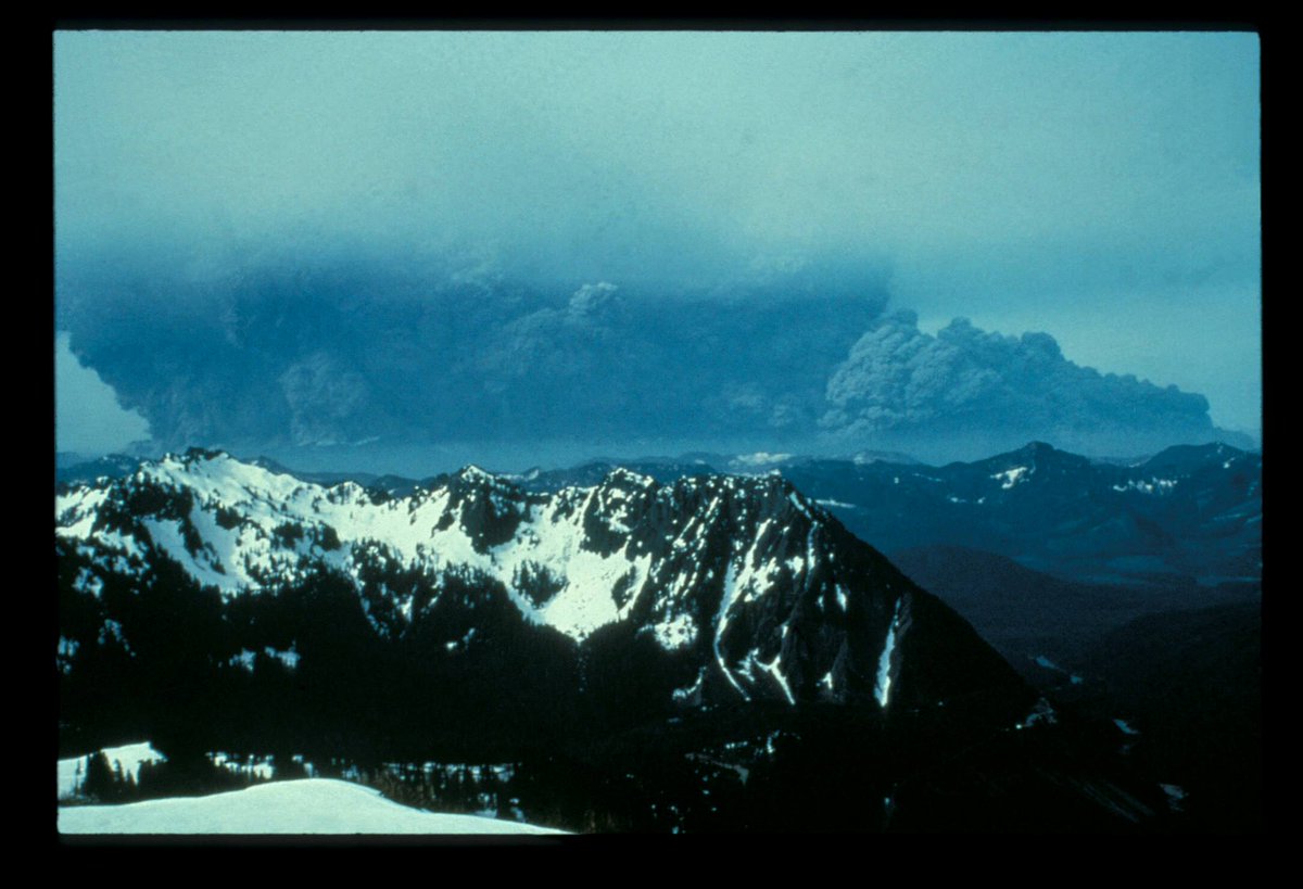 A large cloud of ash billows above a range of mountain peaks.
