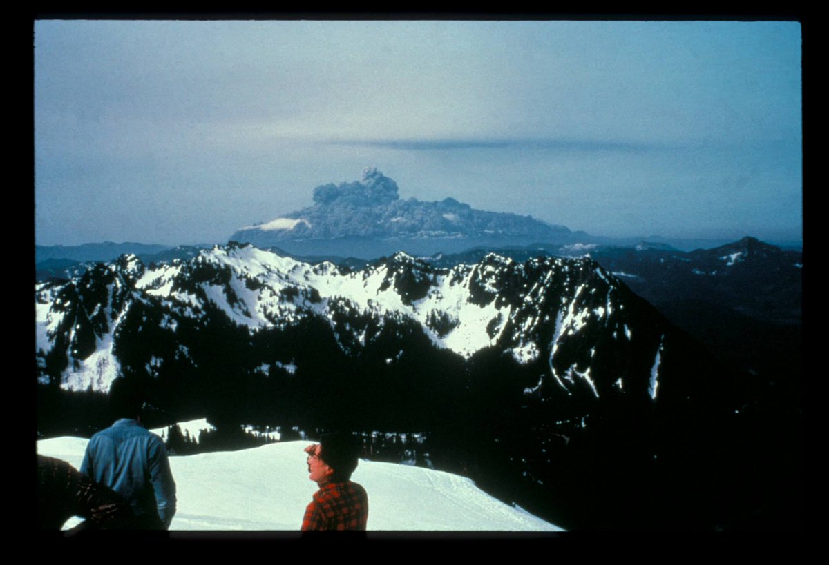 A low cloud of ash wraps around a distant peak.