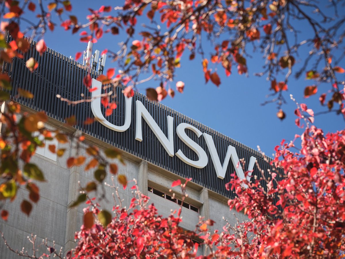 UNSW logo on top of Library building, surrounded by the reds and oranges of Autumn leaves against a blue sky backdrop.