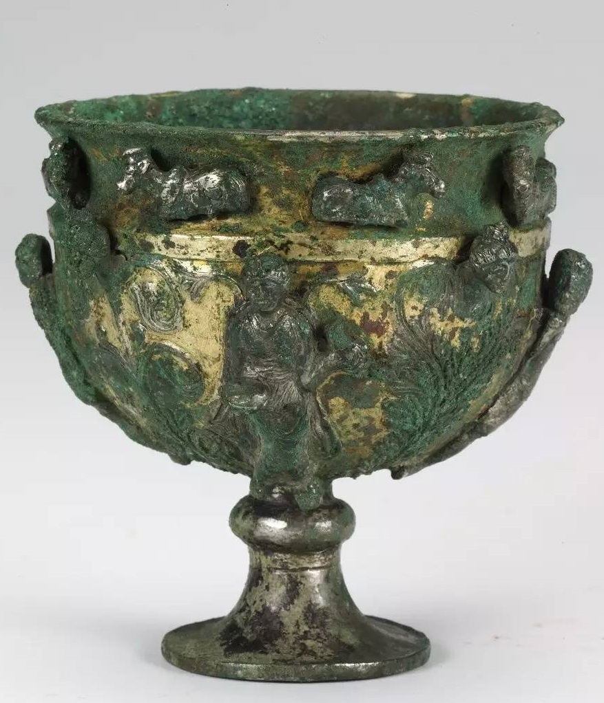 L: Hellenistic-style gilded wine cup decorated with a woman holding a drinking vessel & acanthus leaves, discovered in the foundation of a building at Pingcheng. R: A stem cup from Afganistan or Central Asia. Both the products of Hellenistic art related to the cult of Dionysus.