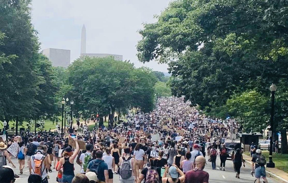 Photo of a large crowd marching in Washington, DC. The Washington Monument is visible in the background.
