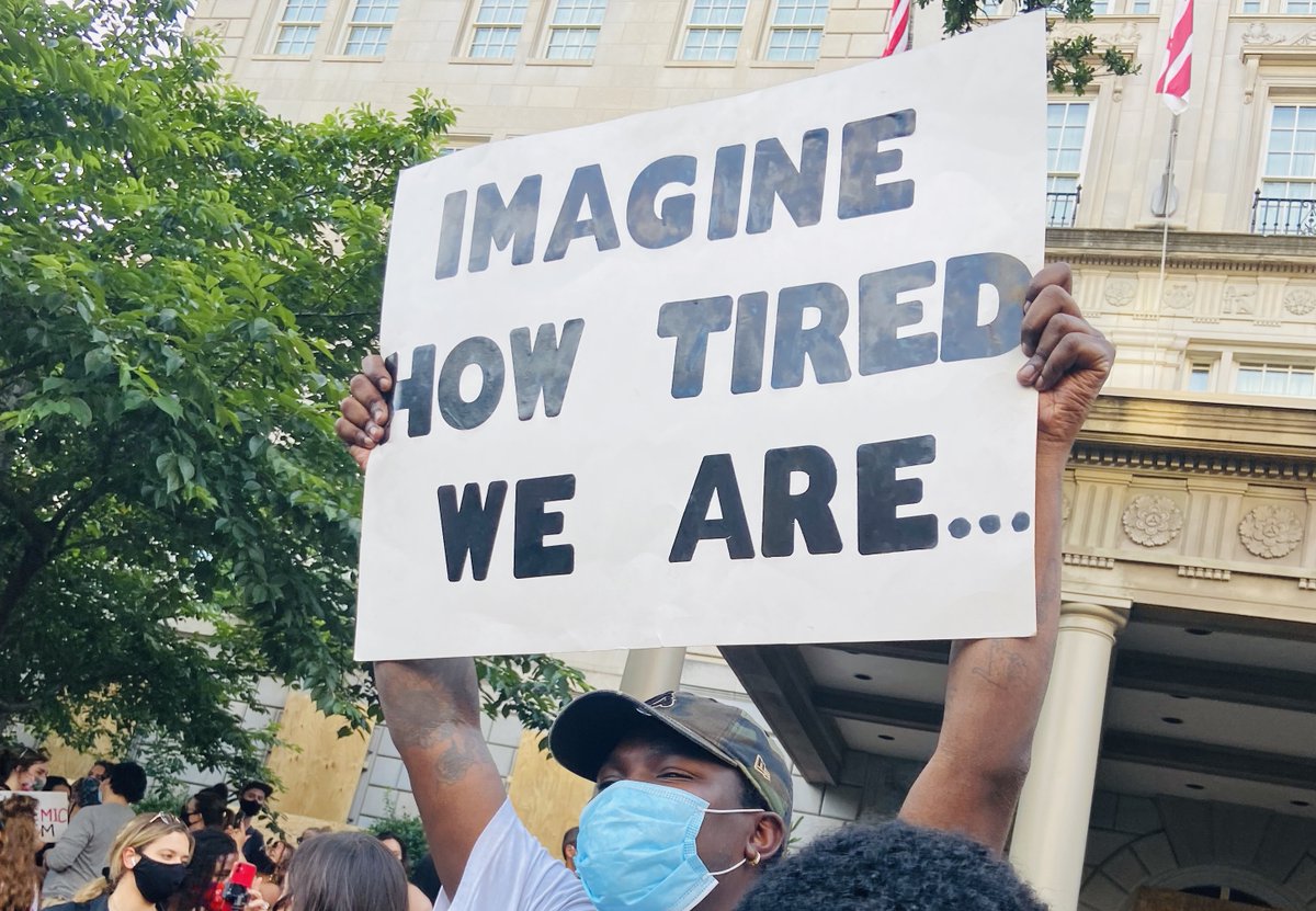 Photo of an African-American man holding up a sign in Washington, DC that says "Imagine how tired we are..."
