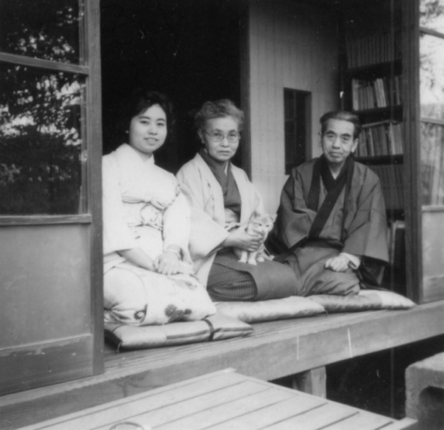 [end quotation]Here is a photo of Chinami with her mother, Magara, and father, Kenji.[image description: A young woman and her parents are kneeling on cushions in front of an open door looking at the camera.]