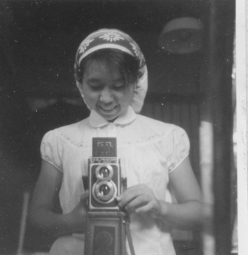 Chinami's effervescent and playful personality was like a window into a better world to me, as was her steadfast commitment to feminism and anarchism. [image description: Chinami stands behind an old camera, smiling and looking down.]
