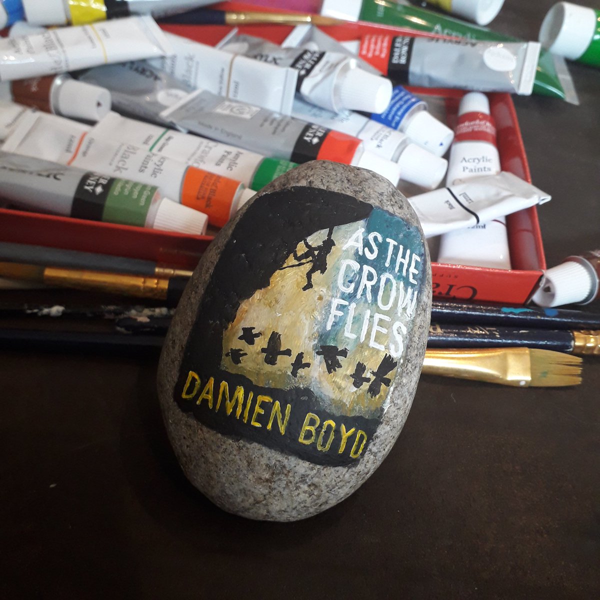 As The Crow Flies by  @DamienBoydBooks painted on a rock to be hidden in my local library