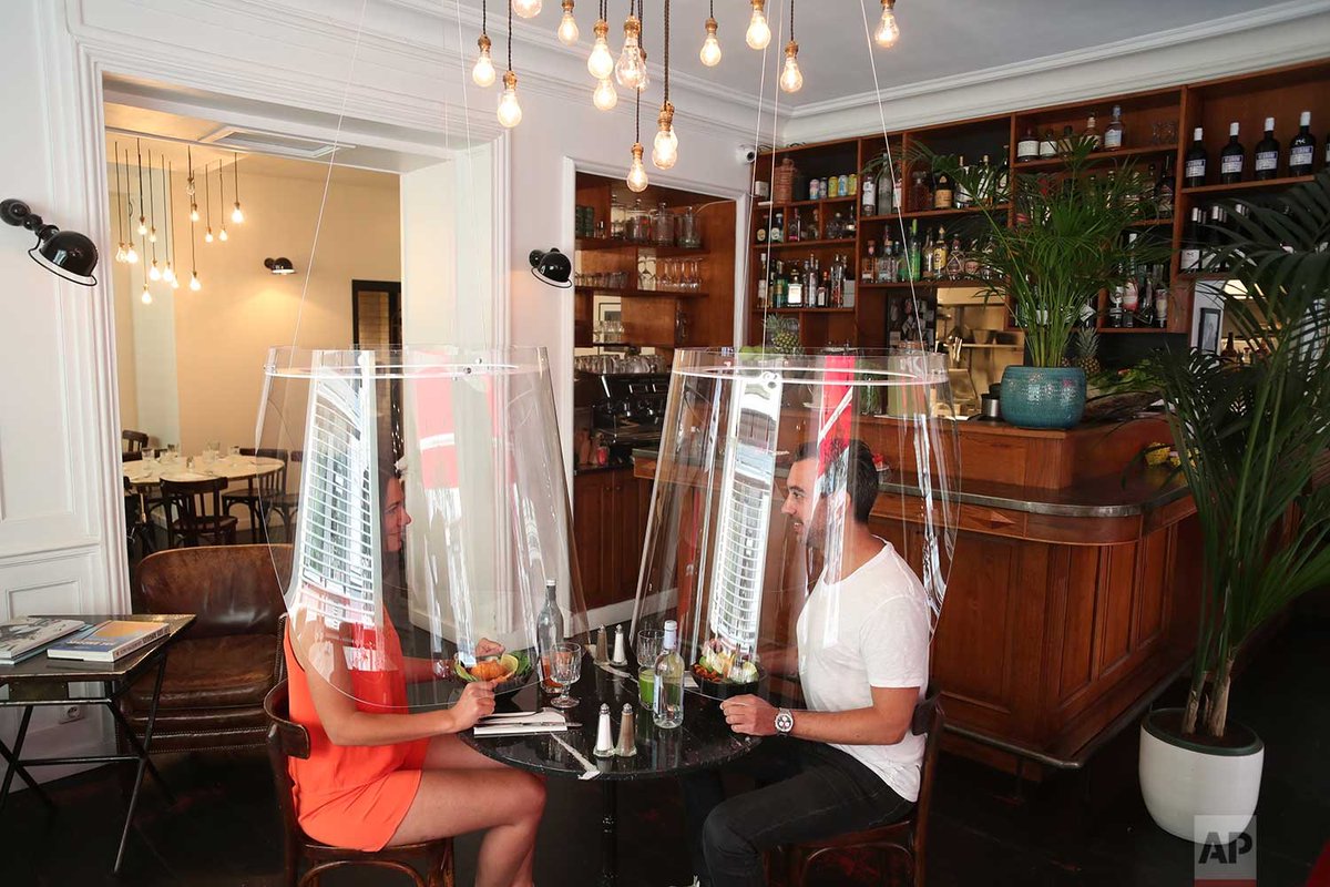 A man and a woman demonstrate dining under a plastic shield in a Paris restaurant on Wednesday, May 27, 2020. As restaurants in food-loving France prepare to reopen, some are investing in lampshade-like plastic shields to protect diners from the virus. | Photo Thibault Camus