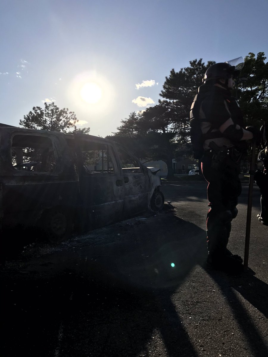 Riot police in front of a destroyed car.