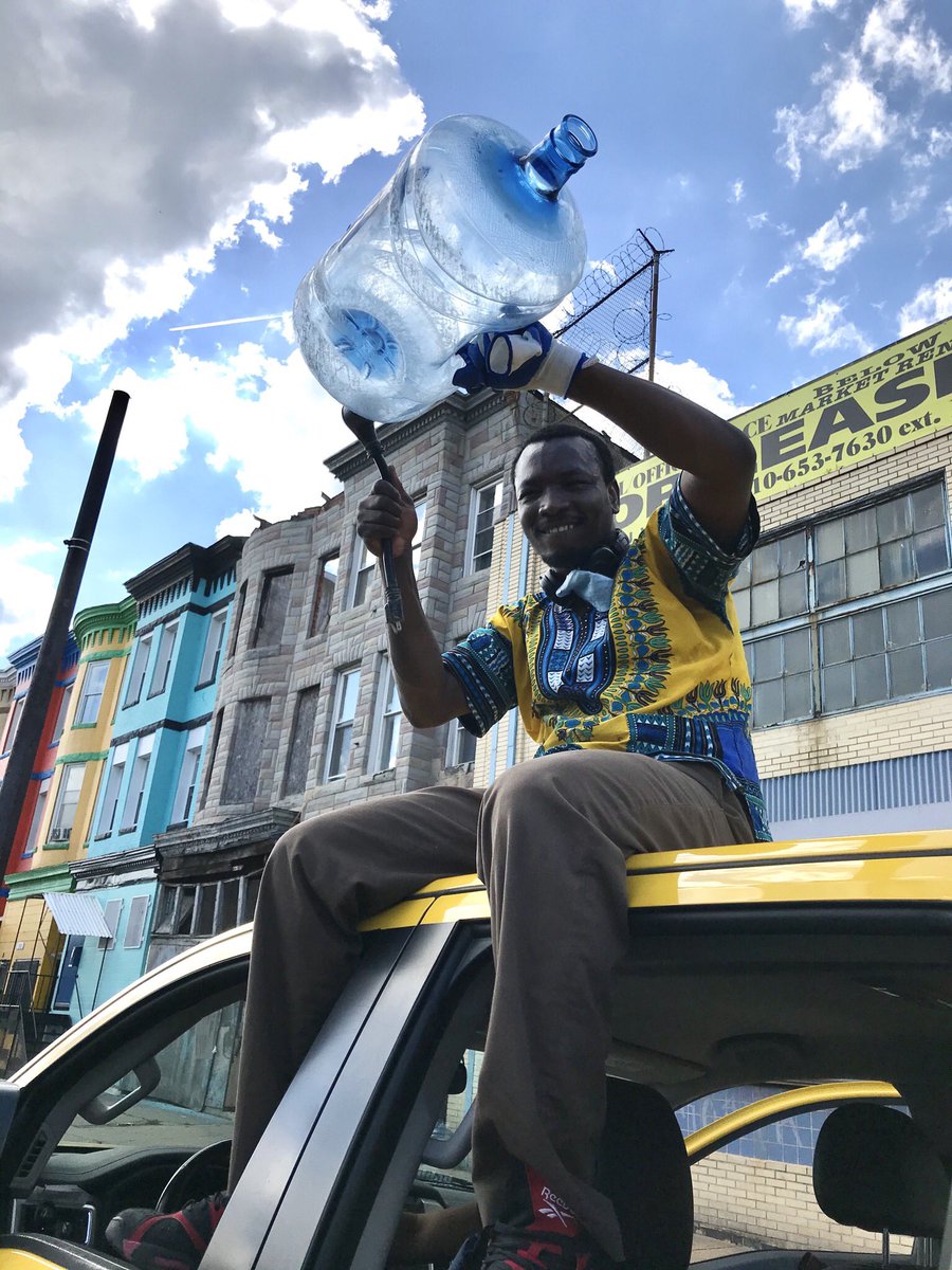 Demba Gologo beats an empty water jug and encourages a car caravan of protesters outside his shop on North Avenue.