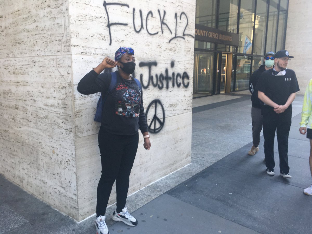 A protester poses for a photo in front of the freshly painted graffiti on a column of the Cook County government building at 69 W Washington in downtown Chicago