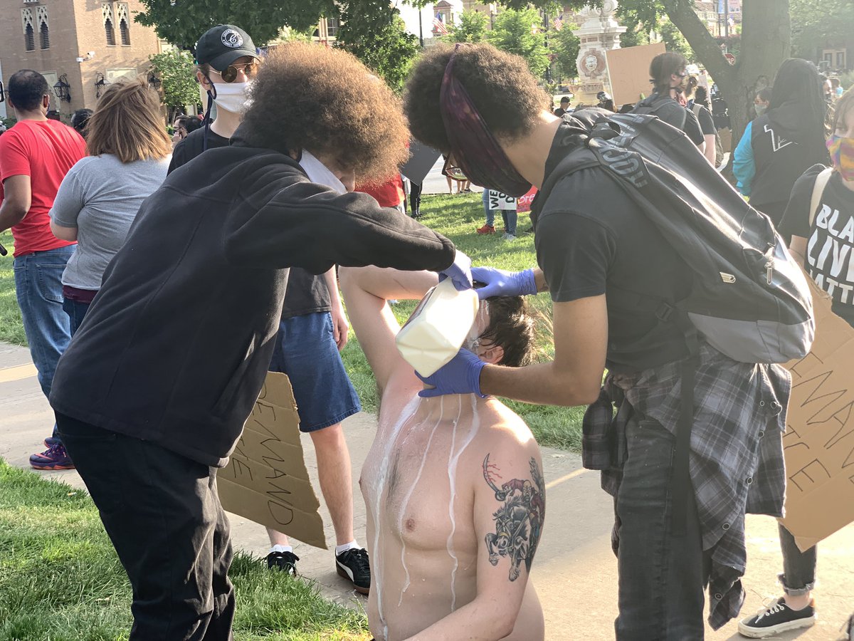 Protesters pour milk on the face of someone who was sprayed.Several containers of bottled water are all over the fountain area, with signs saying “Please Take!”