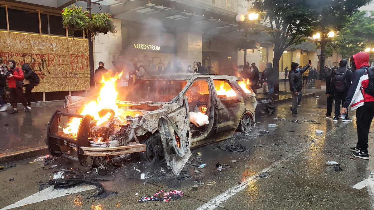 Downtown Seattle smells strongly of tear gas. Sirens ring constantly in the distance. Protesters added a pallet & debris to this car fire. The 5 o'clock downtown curfew has come and gone.  #GeorgeFloydprotest  #seattleprotest – at  Nordstrom Corporate Headquarters