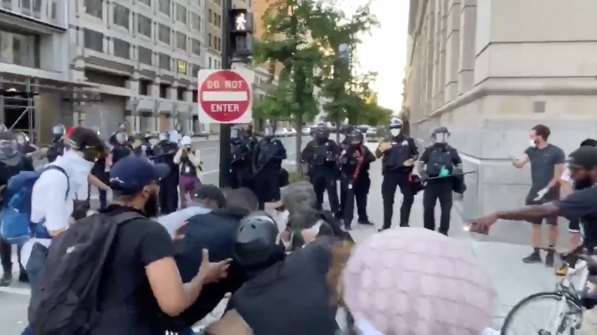 On the left, More Muscle signals to the cops, "Coming in!"On the right, a man in a dark-gray T-shirt tells the cops, "Here they come!" and signals to the team, "Come on in! Everything good!"