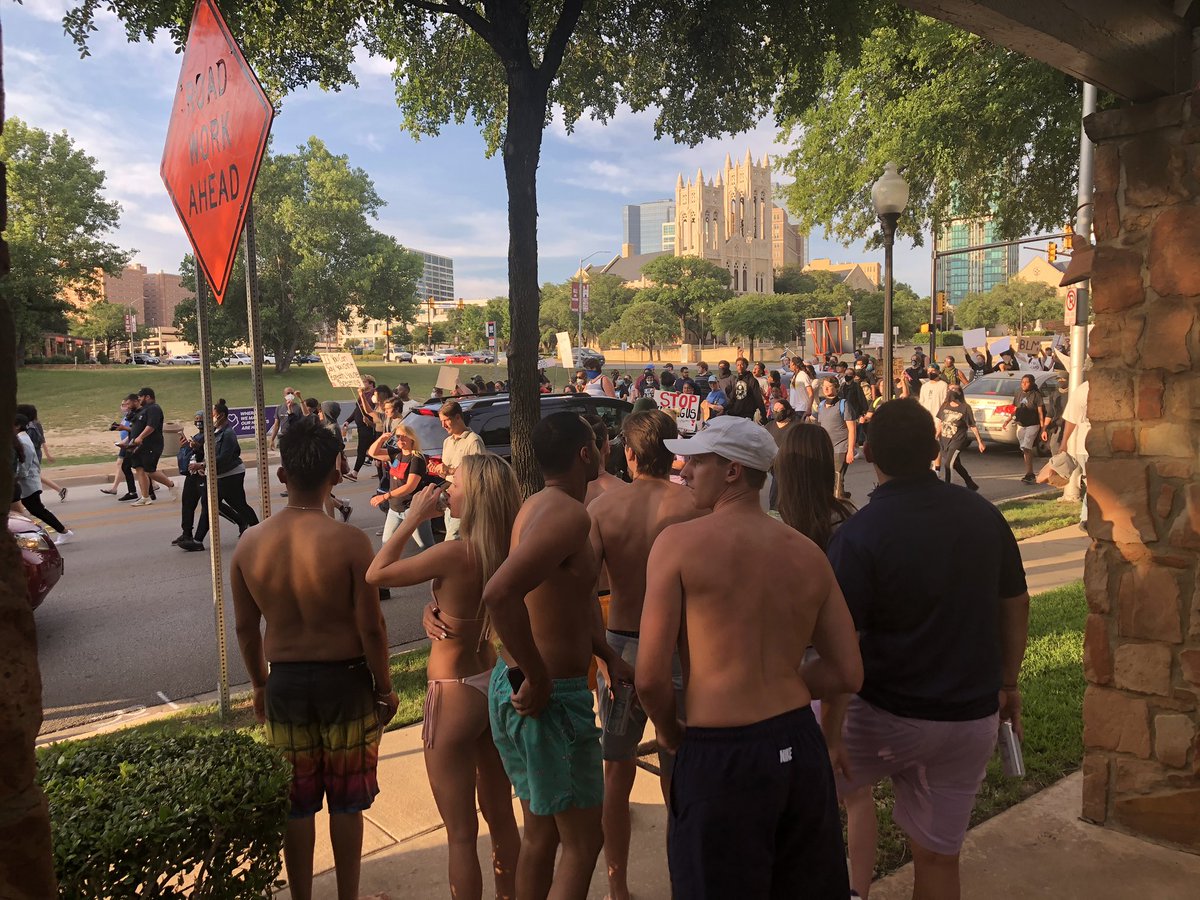 Pool goers at a apartment complex watch as protesters match past. Some marchers yell “use your privilege! Join us !”