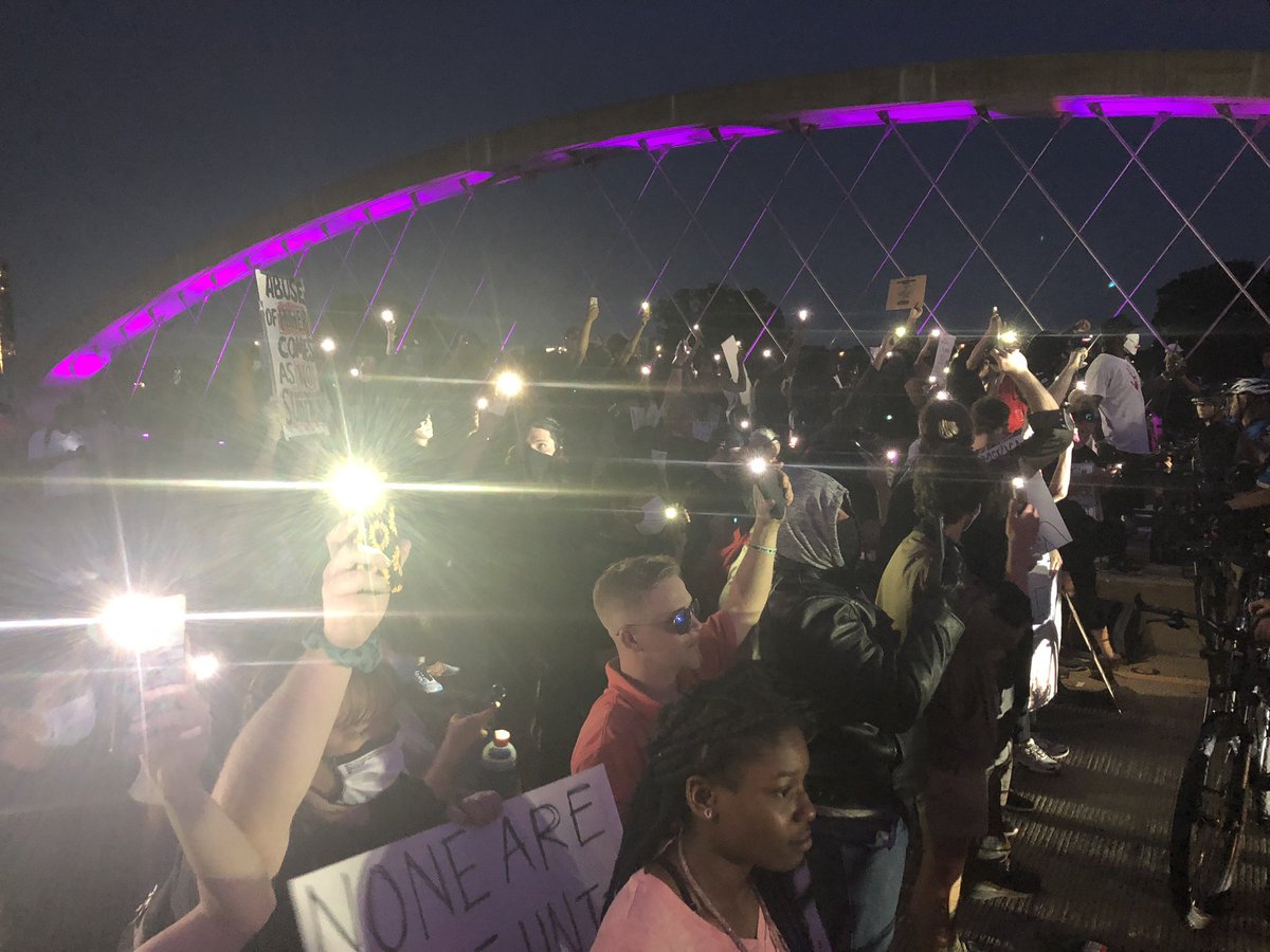 Protesters shout to onlookers, “if you’re woth is, turn your flashlight on!” You can’t see well, but dozens of lights coming from the onlookers now. (Look to the back left in the 2nd photo- that’s people holding phones up)