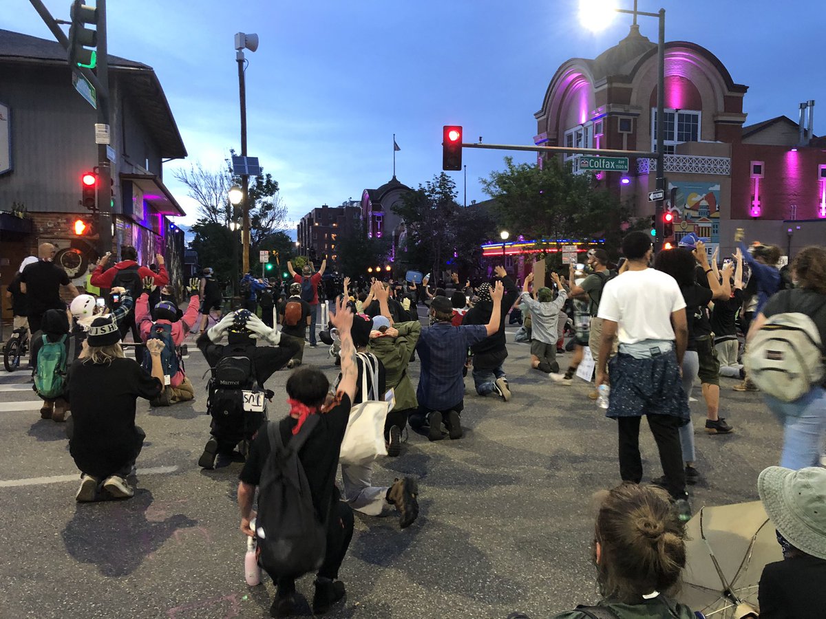 Behind this pack of kneeling people at Colfax and Clarkson is a big line of cops in riot gear, with weapons.