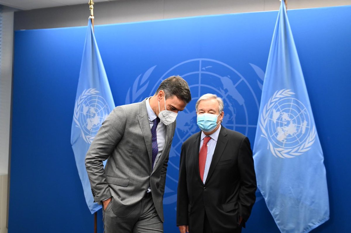 Fotografía del presidente del Gobierno, Pedro Sánchez, y el Secretario General de las Naciones Unidas, António Guterres, delante de un panel azul con el logotipo de las Naciones Unidas y de banderas de ONU. El presidente está levemente agachado mientras escucha a Guterres.