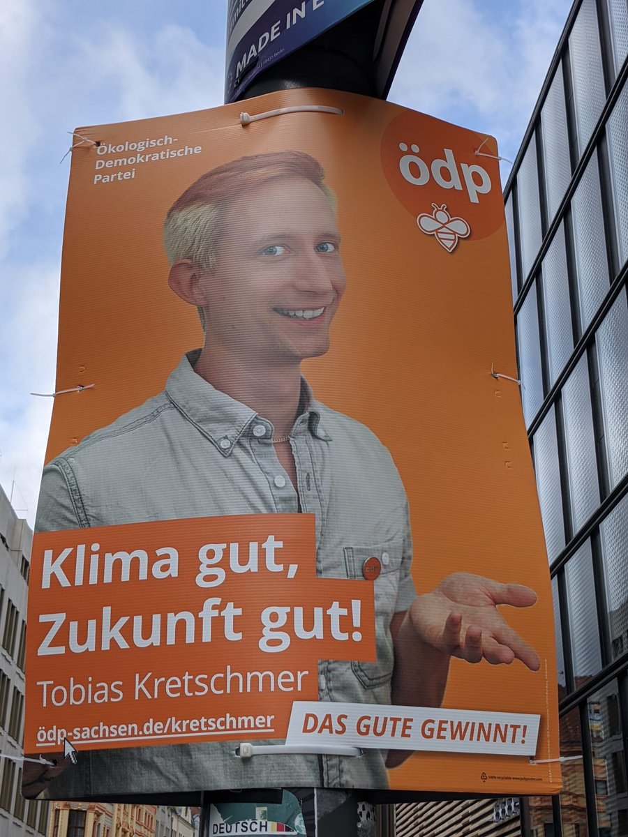 Wahlplakat von Tobias Kretschmer (ödp). Man sieht Portrait des Kandidaten vor orangenem Hintergrund. Seine Haar sind auch orange gefärbt. Er lächelt sehr künstlich und Hände scheinen etwas anzupreisen. Dazu der Claim "Klima gut, Zukunft gut" und "Das Gute gewinnt!" 