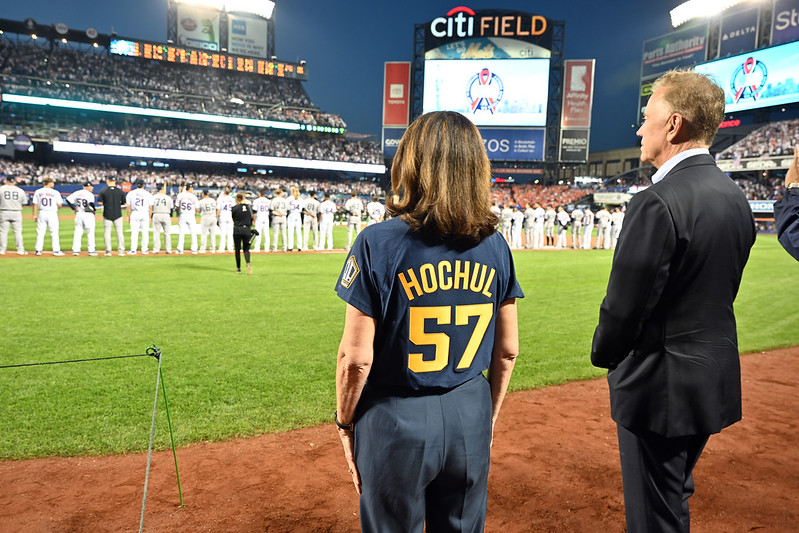 Governor Hochul wearing #57 jersey stands on field with baseball players in background