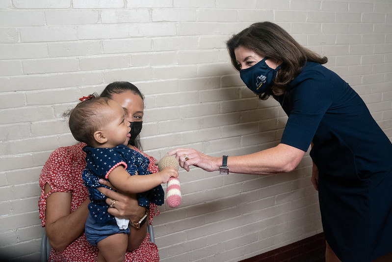 Governor Hochul (right) extends arm to play with baby (left)