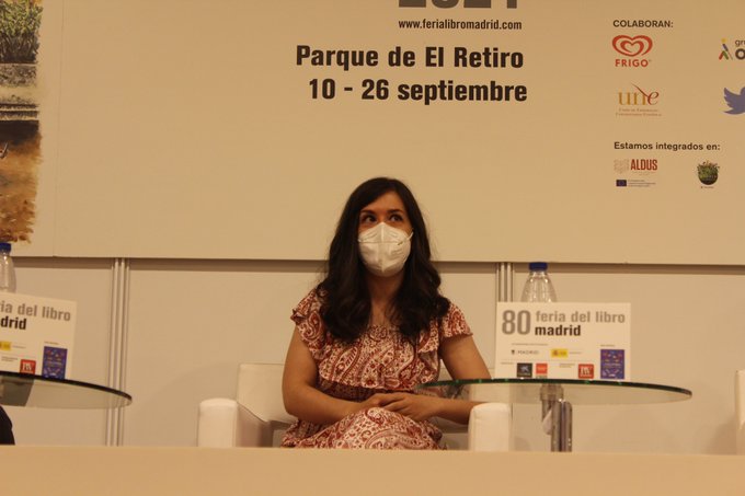 Sonia Lerones mira hacia arriba mientras sus brazos descansan sobre su regazo. Está sentada con las piernas cruzadas sobre un sillón individual blanco. Lleva mascarilla. A la derecha hay una mesa cristal redonda.