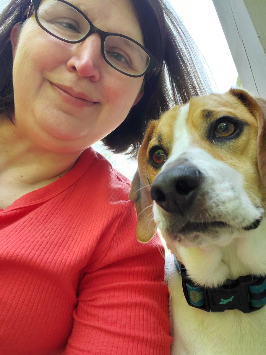 Woman with glasses in red shirt next to a dog.  Beagle mix.