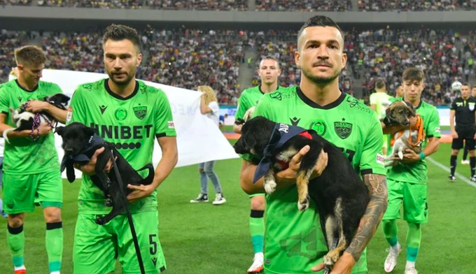 Jogadores do Dínamo de Bucareste carregam cachorrinhos no colo na entrada de campo no fim de semana, em clássico contra o FCSB.