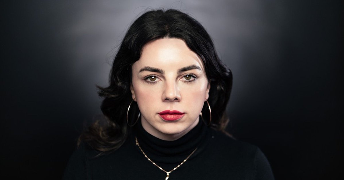 [ID: headshot of Shon Faye, a white trans woman with short wavy black hair, red lipstick, and gold hoop earrings.]