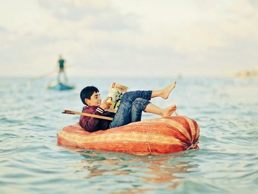 #Gaza City, a Palestinian kid sits on a boat made of plastic bottles and reads his school book at Gaza sea.