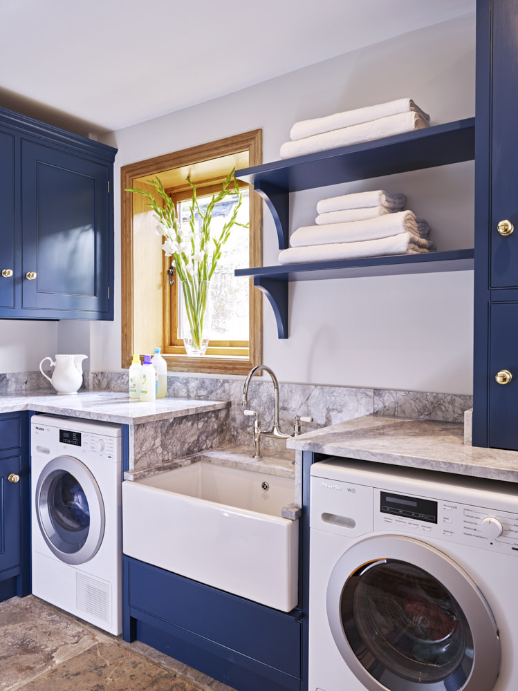 Scullery finished in #stiffkeyblue from Farrow &amp; Ball. The handmade cabinetry houses the Miele laundry appliances, ironing board storage, peg rail for hanging and hides the boiler. An innovative low-set sink with extendable tap, is ideal for filling buckets and washing the dog!