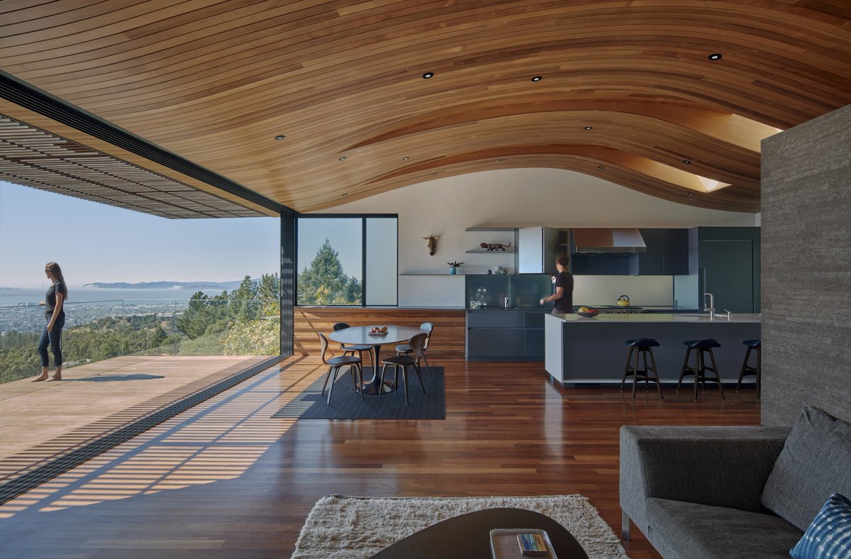 Living space under a curved wooden ceiling opening up to an expansive deck with unobstructed views of San Francisco Bay, Oakland, Alameda County, California