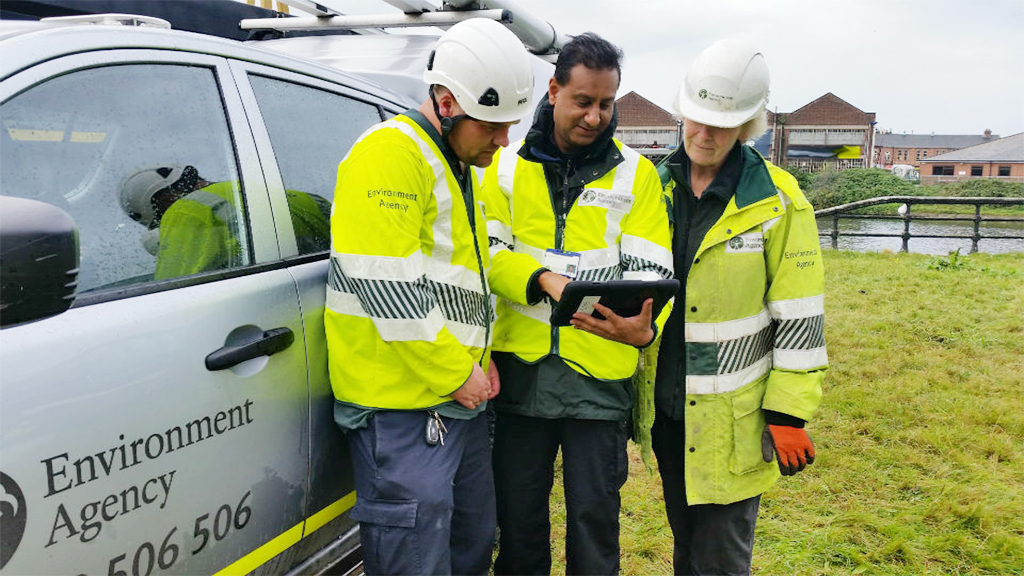 Three people in high vis jackets from Environment Agency gather round an iPad